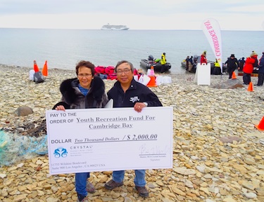 Cambridge Bay Mayor Jeannie Ehaloak and the hamlet's deputy mayor Joe Ohokannoak pose with a giant cheque made out to the local youth recreation fund by Crystal Cruises, Aug. 29 on the beach, with the huge cruise ship in the background. (PHOTO BY JANE GEORGE)