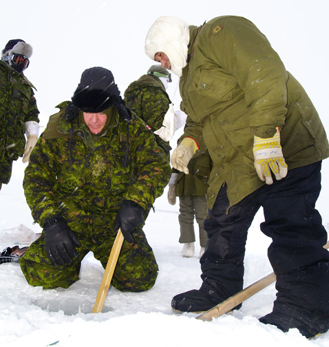 A Canadian Ranger, right, helps a member of the Canadian Forces, left, how to dig a hole for ice fishing in Gjoa Haven in April, 2009. A new study says increased military activity in the Arctic could trigger an arms race in the region. (PHOTO BY CHRIS WINDEYER)