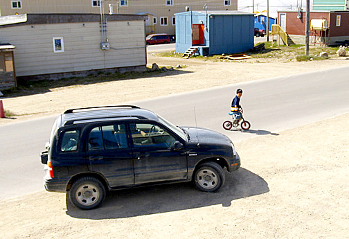 A car passes close to child bicycling on the road in Lower Iqaluit July 9. The city is rolling out an information campaign and installing portable speed bumps to get Iqaluit drivers to slow down around children. (PHOTO BY CHRIS WINDEYER)