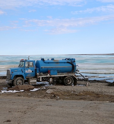 A vacuum truck owned by Kitnuna cleans up oily water at the Cambridge Bay shoreline after a June 14 spill saw about 11,000 litres of waste oil flow down from a tank through the company's yard. (PHOTO BY RED SUN PRODUCTIONS)