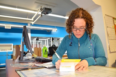 Alia Bigro, a volunteer at Atii fitness, works at the front desk. There are currently 53 volunteers at the gym, which includes 18 board members, 21 desk volunteers, 11 instructors and personal trainers, and five ancillary volunteers — some do double duty and have roles at the gym. (PHOTO BY DAVID MURPHY)  