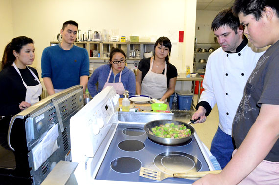 Members of the Skills Nunavut Iqaluit cooking club from left, Nicole Amagoalik, Simeonie Kisa-Knickelbein, Madeline Allakariallak, Tooma Laisa and Shawn Baines (at right) gathered Dec. 11 to hear instructor Aaron Watson, second from right, explain how to prepare lemon brussel sprouts with bacon lardon and walnuts. (PHOTO BY JIM BELL) 