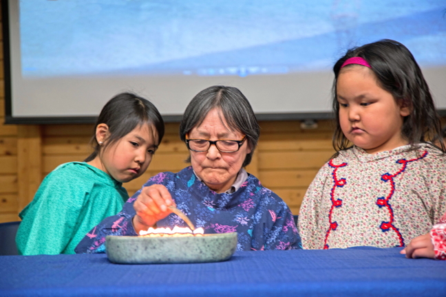 Cambridge Bay elder Mary Avalak, flanked by her grandchildren, lights the qulliq to begin a community feast April 17 organized by the Arctic Research Foundation. (PHOTO BY DENISE LEBLEU IMAGES)