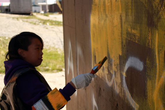 Anna Kanayuk covers up the F-word with some bright yellow paint last week in Puvirnituq. (PHOTO COURTESY OF PIVALLIANIQ)