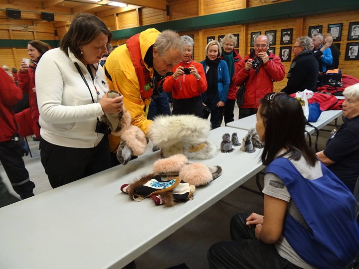 A passenger from the Hapag-Lloyd cruise ship the Bremen eyes some wolf fur mittens for sale at the Cambridge Bay community hall during a stop in that community Aug. 31. The western Nunavut hub has been busy this week hosting passengers from several cruise ships and private yachts. According to local cruise coordinator Vicki Aitaok, passengers from the giant Crystal Serenity ship, which stopped in Cambridge Bay Aug. 29, dropped about $100,000 in the community in goods, donations and shore services. The smaller Bremen, carrying about 150 mainly German passengers, was mid-way through a 20-day round-trip Northwest Passage voyage starting and ending in Greenland. Read more about that ship's port of call on nunatsiaqonline.ca. (PHOTO BY JANE GEORGE)
