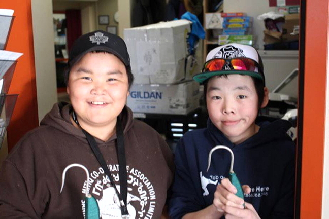 Simeonie Uppik, left, and Johnassie Sala hold up nitsiit that they made in shop class at Paatsaali School in Sanikiluaq. Nitsiit are used by hunters to hook seals, beluga and other marine animals out of the water during harvesting. Paatsaali's shop class teachers often get students to make traditional tools including harpoons, qamutiks, fishnets, kakivaks and ulus. Students also learn small engine repair on snowmobiles and all-terrain vehicles. (PHOTO COURTESY PAATSAALI SCHOOL)