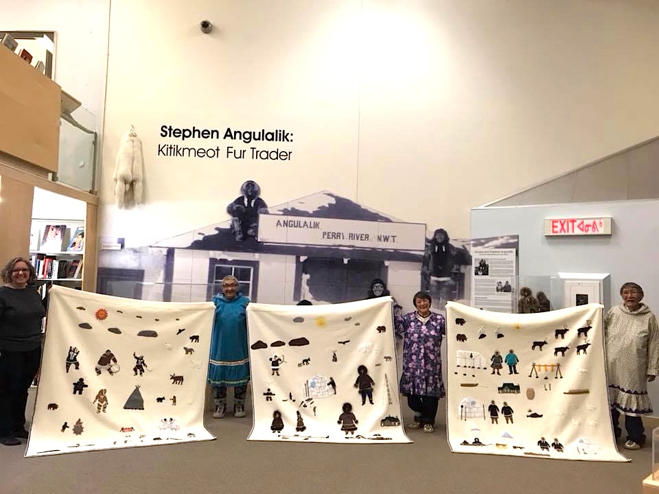 Jacqueline Lalonde, at the left, of Indigenous and Northern Affairs Canada, accepts three wall-hangings that were created over eight months by the elders in residence at the Kitikmeot Heritage Society in Cambridge Bay for the Canadian High Arctic Research Station. From left, you can see the wall hangings and their creators—life in Cambridge Bay 100 years ago, with Annie Atighioyak; life in Cambridge Bay 50 years ago, with Mary Avalak; and, life in Cambridge Bay today, with Mabel Etegik. 